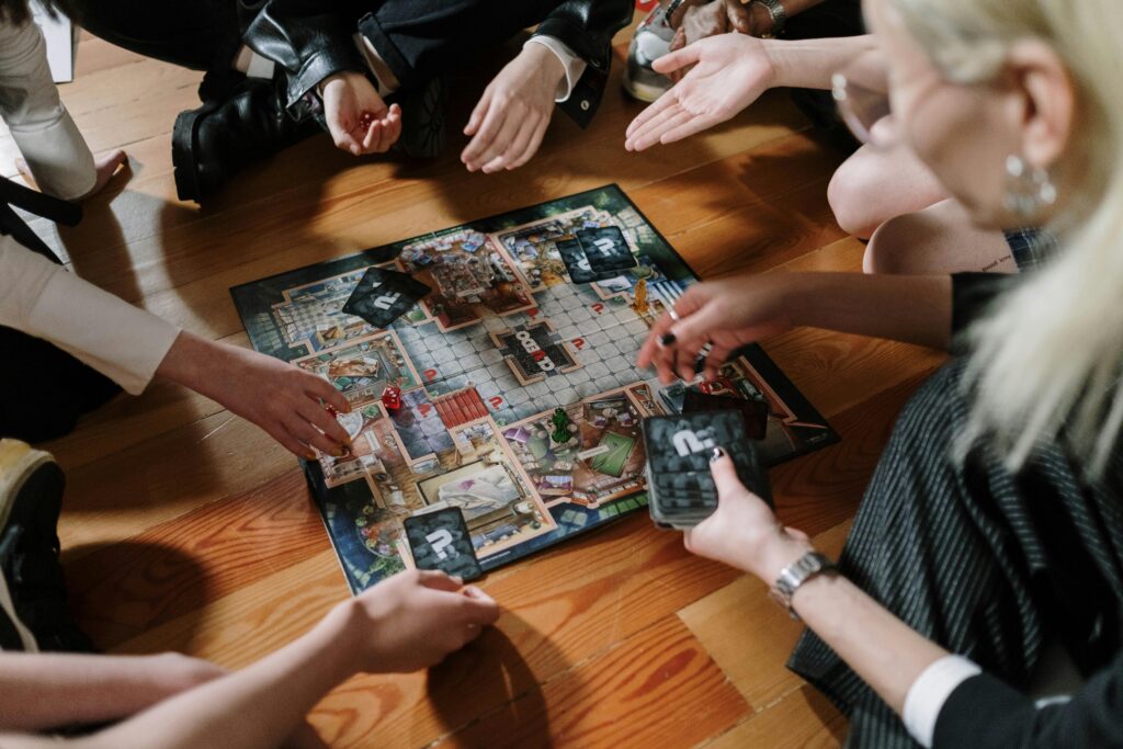 Group of adults enjoying a board game session indoors, casually gathered on wooden floor.
